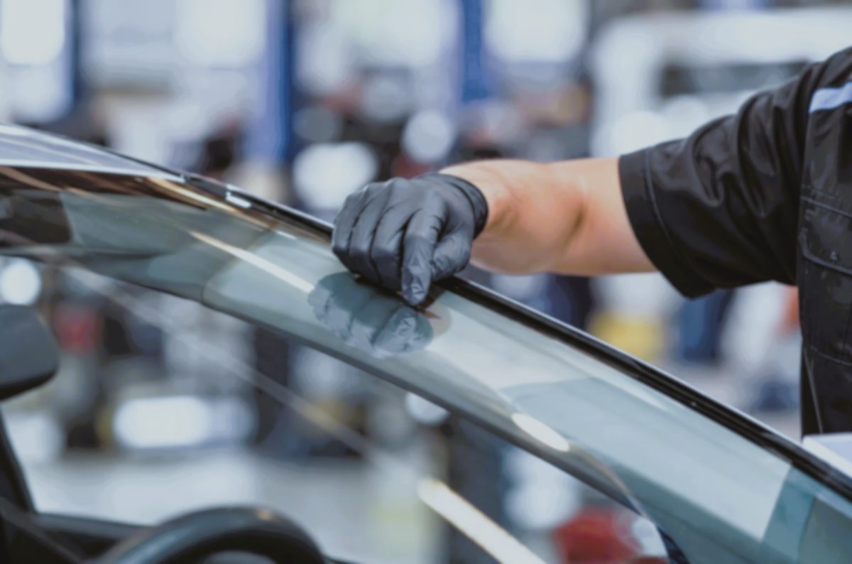Technician in gloves fitting a new windscreen to a car in a workshop